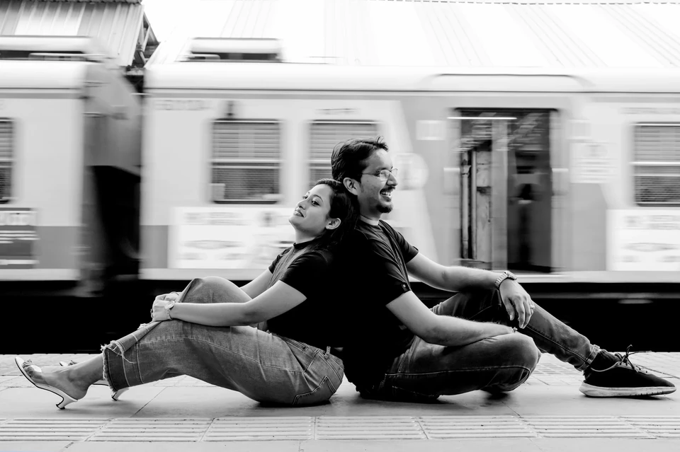 Couple sitting back to back beside a moving train in black and white